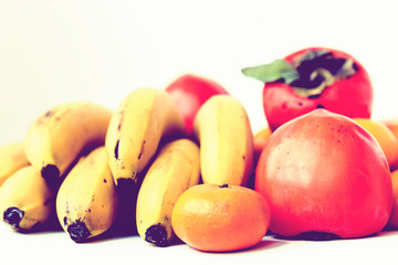 A selection of arranged different fresh fruits of bananas, mandarins, persimmons and lemons on white background close up.