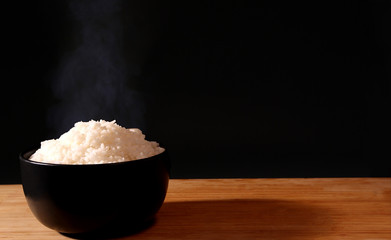 Rice in a black bowl and smoke on a black background.