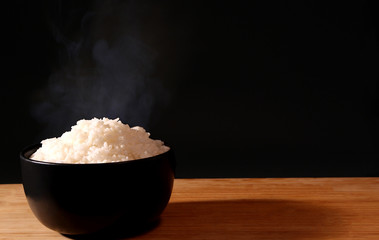 Rice in a black bowl and smoke on a black background.