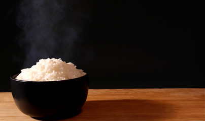 Rice in a black bowl and smoke on a black background.