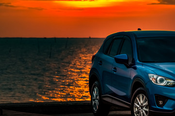 Fototapeta na wymiar Blue compact SUV car with sport and modern design parked on concrete road by the sea at sunset in the evening. Hybrid and electric car technology concept. Car parking space. Automotive industry.