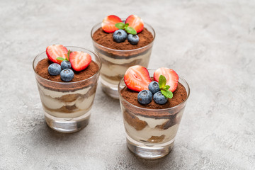 Classic tiramisu dessert with blueberries and strawberries in a glass on concrete background