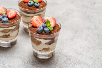 Classic tiramisu dessert with blueberries and strawberries in a glass on concrete background