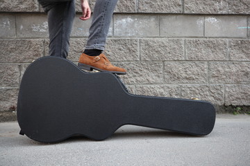 man put his foot on a hard guitar case. hard case for electric guitar. Man dressed in jeans holding guitar case against wall. guy with a guitar. copy space text