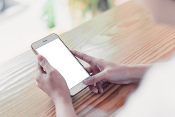 Mock up croppes shot women hand holding white smartphone with blank screen on wooden counter bar in cafe. vintage tone for business technology background concept. closeup mobile.