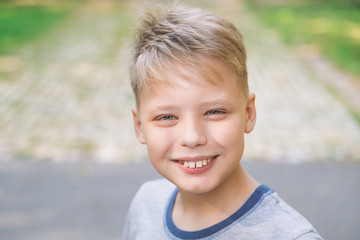 Closeup portrait of happy smiling candid face of white handsome kid standing outdoors in green sunny park. Horizontal color photography.