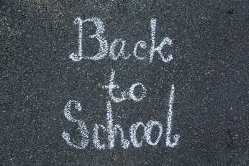 Fototapeta na wymiar Closeup top view of phrase Back to school drawn with white chalk on grey surface of sidewalk. Horizontal color photography.