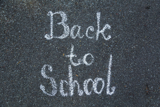Closeup top view of phrase Back to school drawn with white chalk on grey surface of sidewalk. Horizontal color photography.