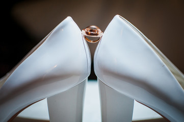 Pair of golden wedding rings between pair of a white shoes