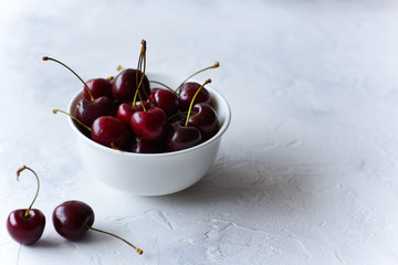 Red sweet cherries in a white bowl on a white surface.