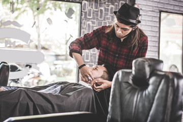 close up portrait of Asian barber with long hair shaving his costumer hair at barbershop