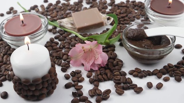 Accessories for spa and aromatherapy with coffee as the main ingredient.  Burning candle, pink lily, coffee soap in the seashells and coffee hand scrub in glass bowl on a white background