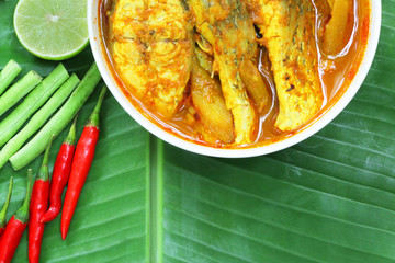 Yellow curry snapper fish with Lotus Stems, Southern Thai Spicy food and fresh vegetable in white dish on banana leaf / selective focus