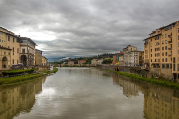 Fototapeta na wymiar Italy, Florence, the capital of Tuscany. View from the Ponte Vecchio on the Arno River and the surrounding urban areas. Pre-storm May sky.