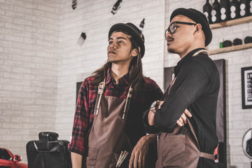portrait of two stylist barber hairdresser with apron standing at barbershop.