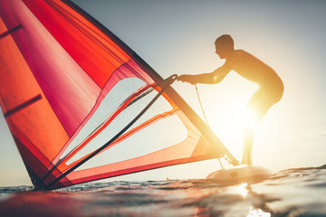 Young man uplift sail for windsurfing on sunset sea
