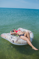 European slim girl in a red bikini swims in the ocean on an inflatable mattress in sunglasses