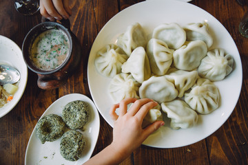 Table served with georgian dishes including hinkali, pkhali and soup. Kind's hand taking one of the hinkali