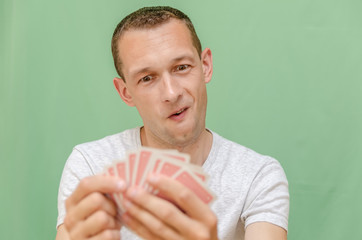 A man on a green background looks at his cards and smiles, a good card in poker. Focus on man