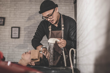 portrait of barber washes costumer hair who relaxed in the chair sink