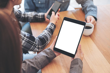 A woman using and looking at mockup tablet pc on wooden table with friends in background