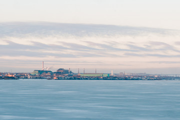 Obraz premium landscape of frozen sea with plants on the horizon. industrial city on the background of the sea in winter. beautiful winter seascape