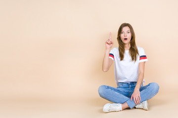 Young woman with crossed legs sitting on pastel beige background