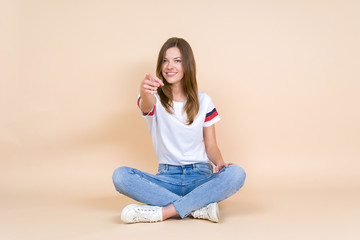Young woman with crossed legs sitting on pastel beige background