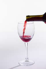 Red wine pouring into glass from bottle on white background