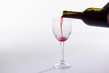 Red wine pouring from bottle into big glass on white background with copy space