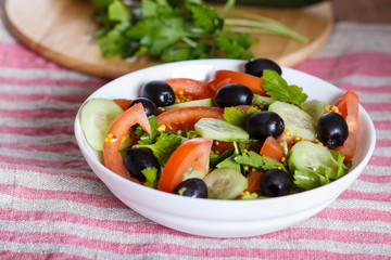 Vegetarian salad of tomatoes, cucumbers, parsley, olives and mustard on linen tablecloth.
