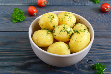 Tasty boiled young potatoes with butter and dill in a bowl on a dark background.