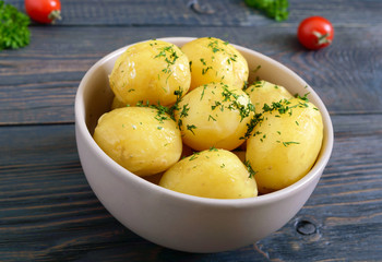 Tasty boiled young potatoes with butter and dill in a bowl on a dark background.