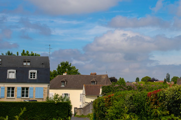 Fototapeta na wymiar Blue cloudy and contrasting sky over a European village. French country houses. Hedge and lots of greenery down the alley.