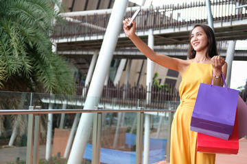 woman holding shopping bags taking selfie with smartphone. consumerism lifestyle in mall