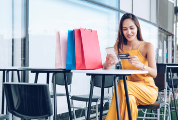 woman holding mobile smart phone & credit card for online payment with shopping bags on table. consumerism lifestyle concept