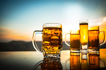 Glass of beer on a beach at sunset. Cooling summer drink concept. Close Up of A Glass of Draught Beer with the Bokeh of Sunlight Background