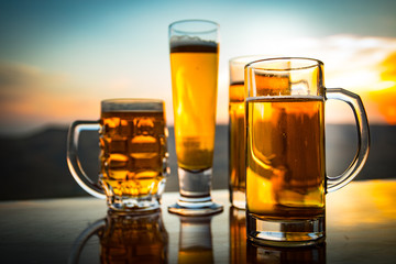 Glass of beer on a beach at sunset. Cooling summer drink concept. Close Up of A Glass of Draught Beer with the Bokeh of Sunlight Background