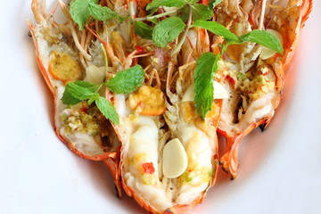 Top view, close up grilled fresh river shrimp with seafood sauce, slice garlic and mint leaves in white plate is famous food in Thailand look delicious.