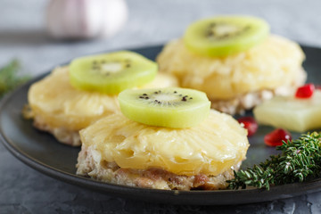 Pieces of baked pork with pineapple, cheese and kiwi on gray background.