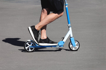 Man in shorts rides blue scooter in park. Outdoor activities