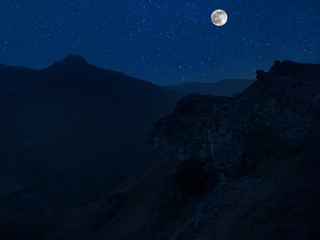 Mountain Road through the forest on a full moon night. Scenic night landscape of country road at night with large moon. Long shutter photo