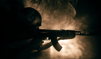 Silhouette of man with assault rifle ready to attack on dark toned foggy background or dangerous...