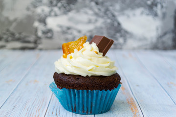 Chocolate cupcakes with vanilla butter frosting and golden crumbs, chocolate, and lemon. There is a memo for the text. Wooden light background.
