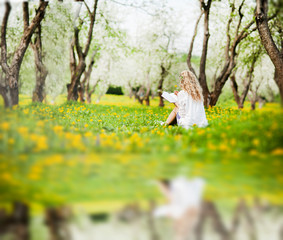 young beautiful blonde girl with beautiful hair sits in the park with a book and a flower in her hands