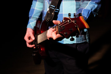 Hands of man playing electric guitar in red light. Bend technique