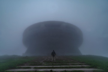 Man is standing in front of abandoned communist monument Buzludzha hidden in deep fog in Bulgaria