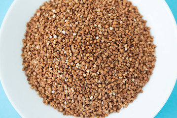 Plate with raw buckwheat on a blue background
