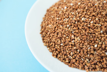 Plate with raw buckwheat on a blue background