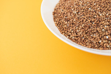 Plate with raw buckwheat on yellow background